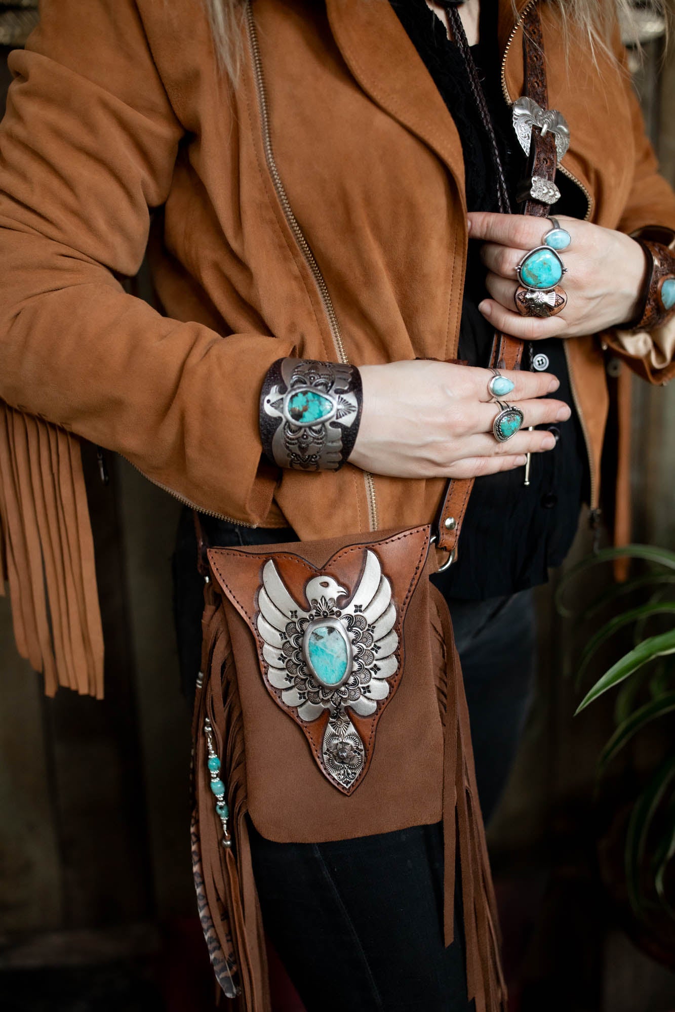 Person wearing a brown jacket with turquoise jewelry and a decorative belt bag.