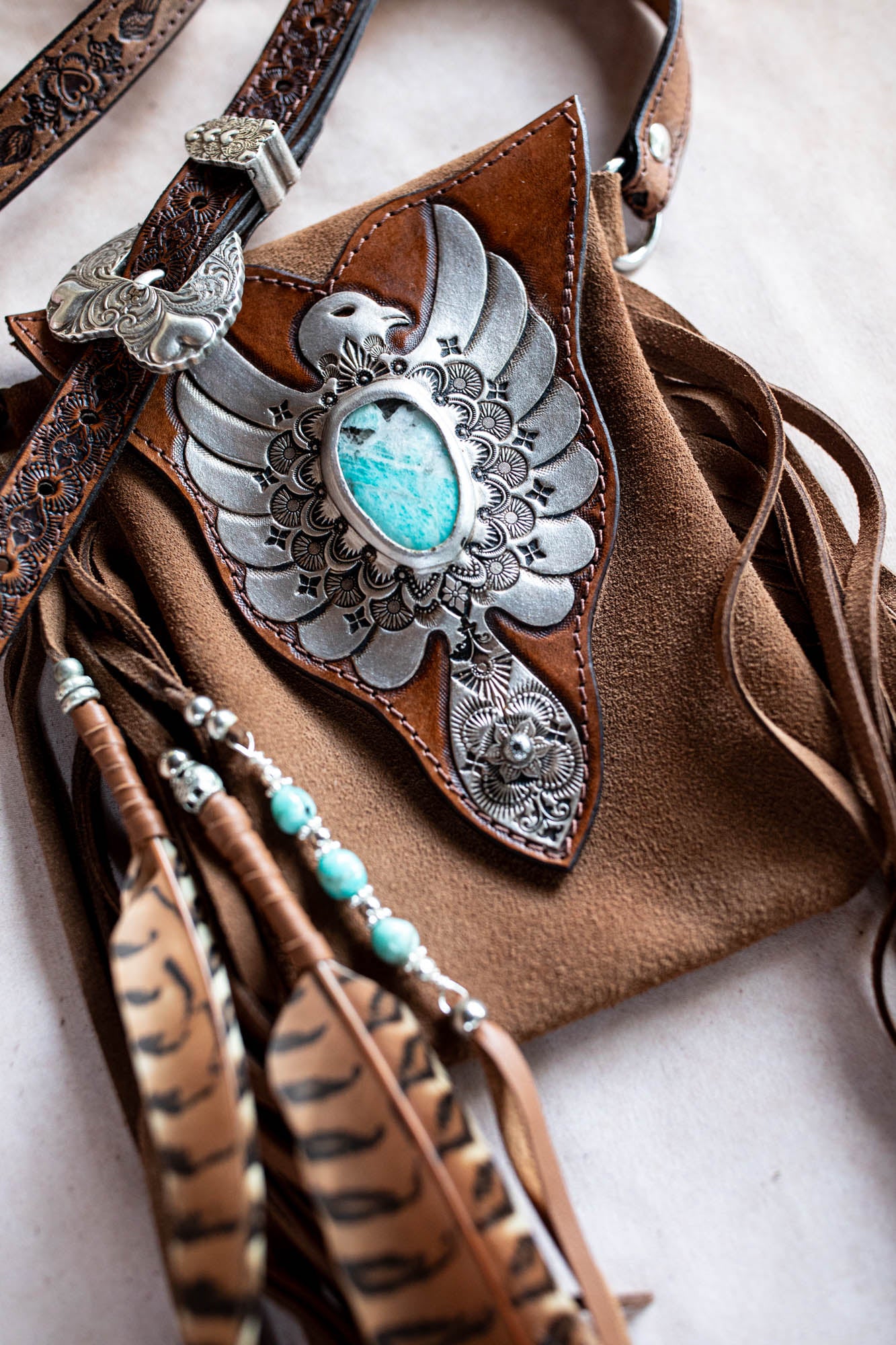 Brown leather bag with decorative silver and turquoise emblem on a light background