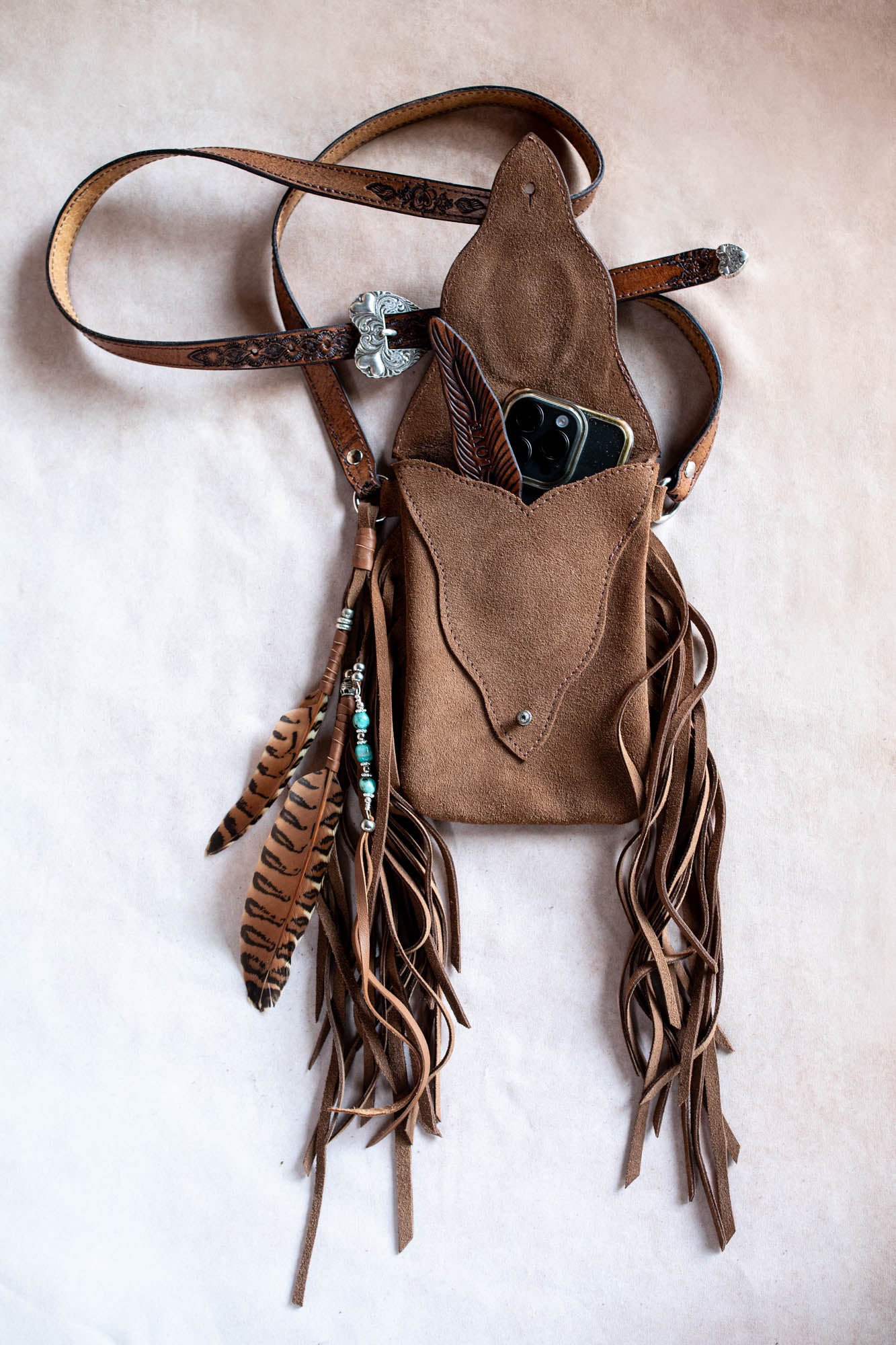 Brown leather bag with fringe and decorative elements on a beige background