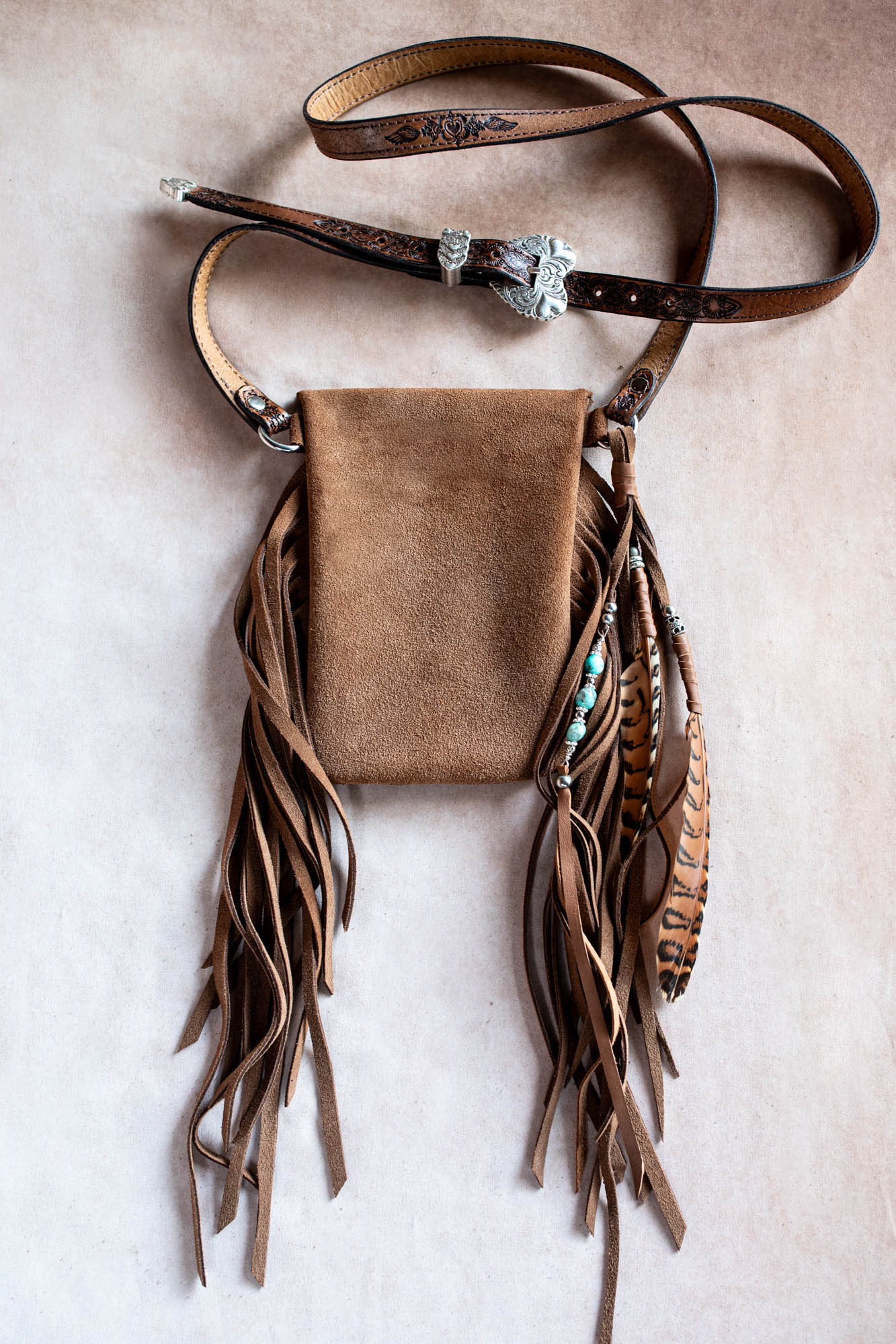 Brown leather bag with fringe and decorative elements on a beige background